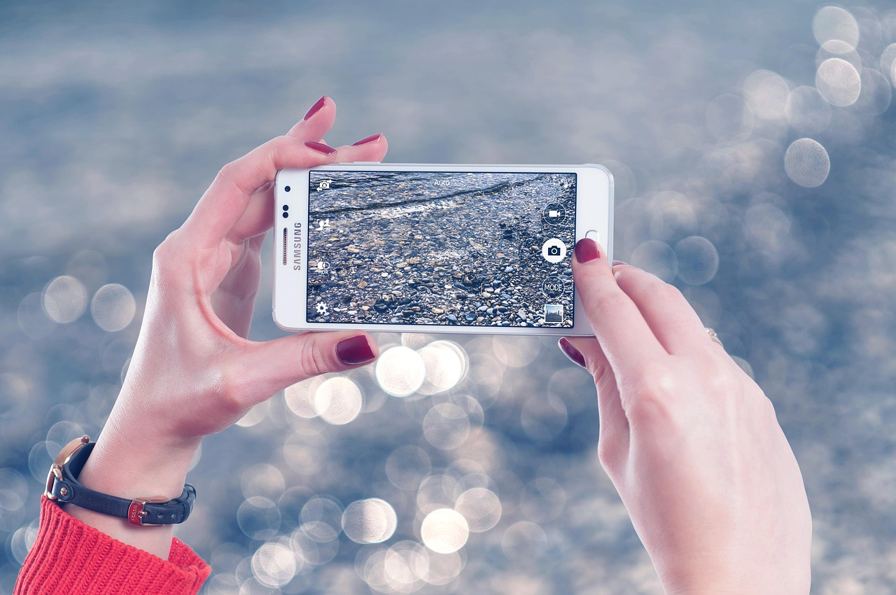 Deux mains tiennent un smartphone à l'horizontale pour prendre une photo, sur un fond clair flou