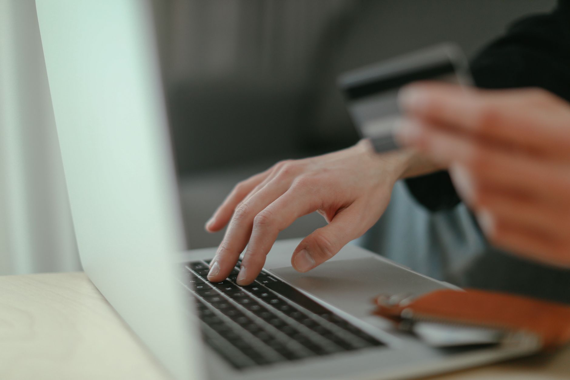Mains d’une personne tenant une carte bancaire tout en utilisant le clavier d’un ordinateur portable.