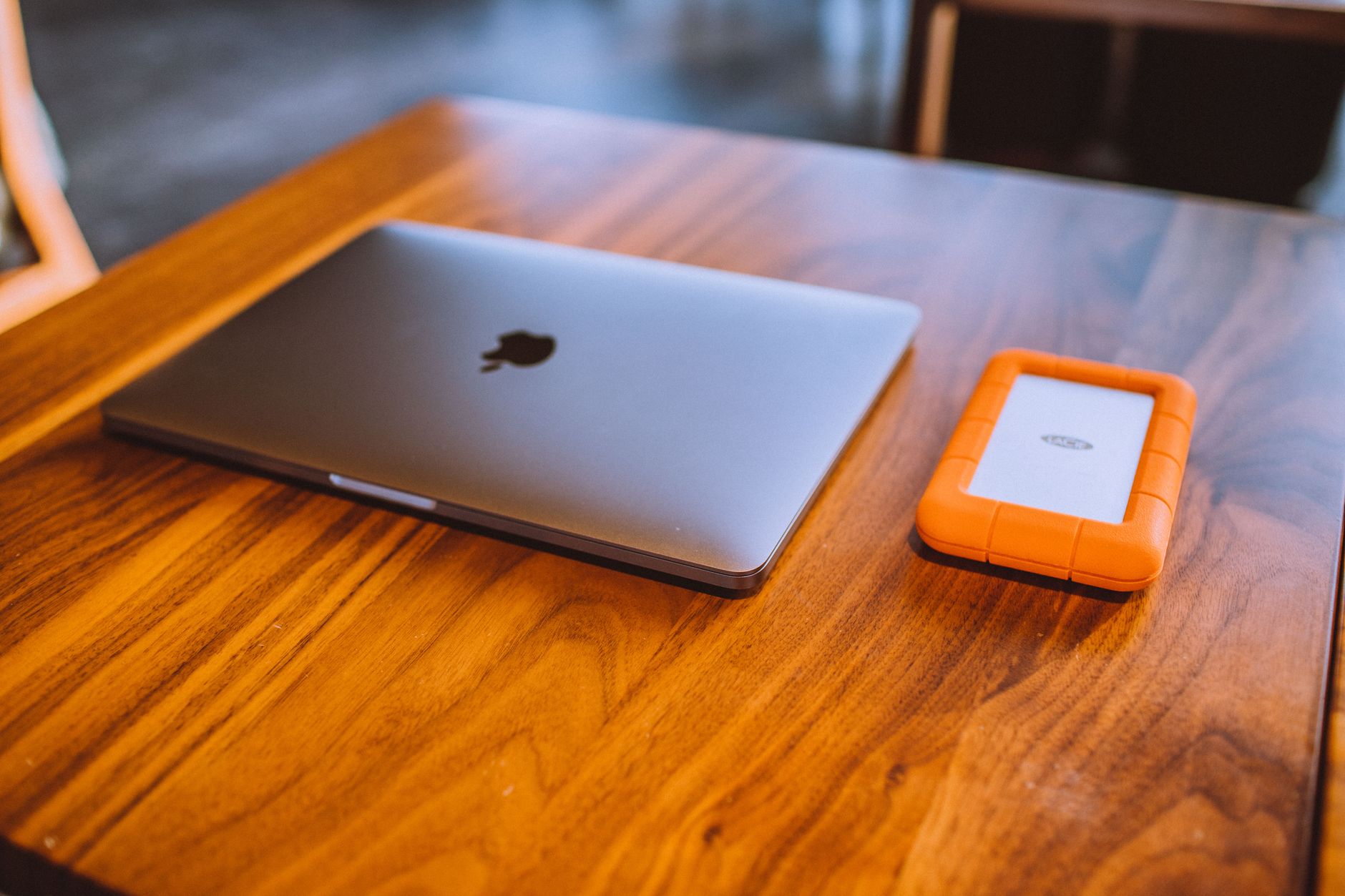 Ordinateur portable fermé et disque dur externe à coque orange posés sur une table en bois.