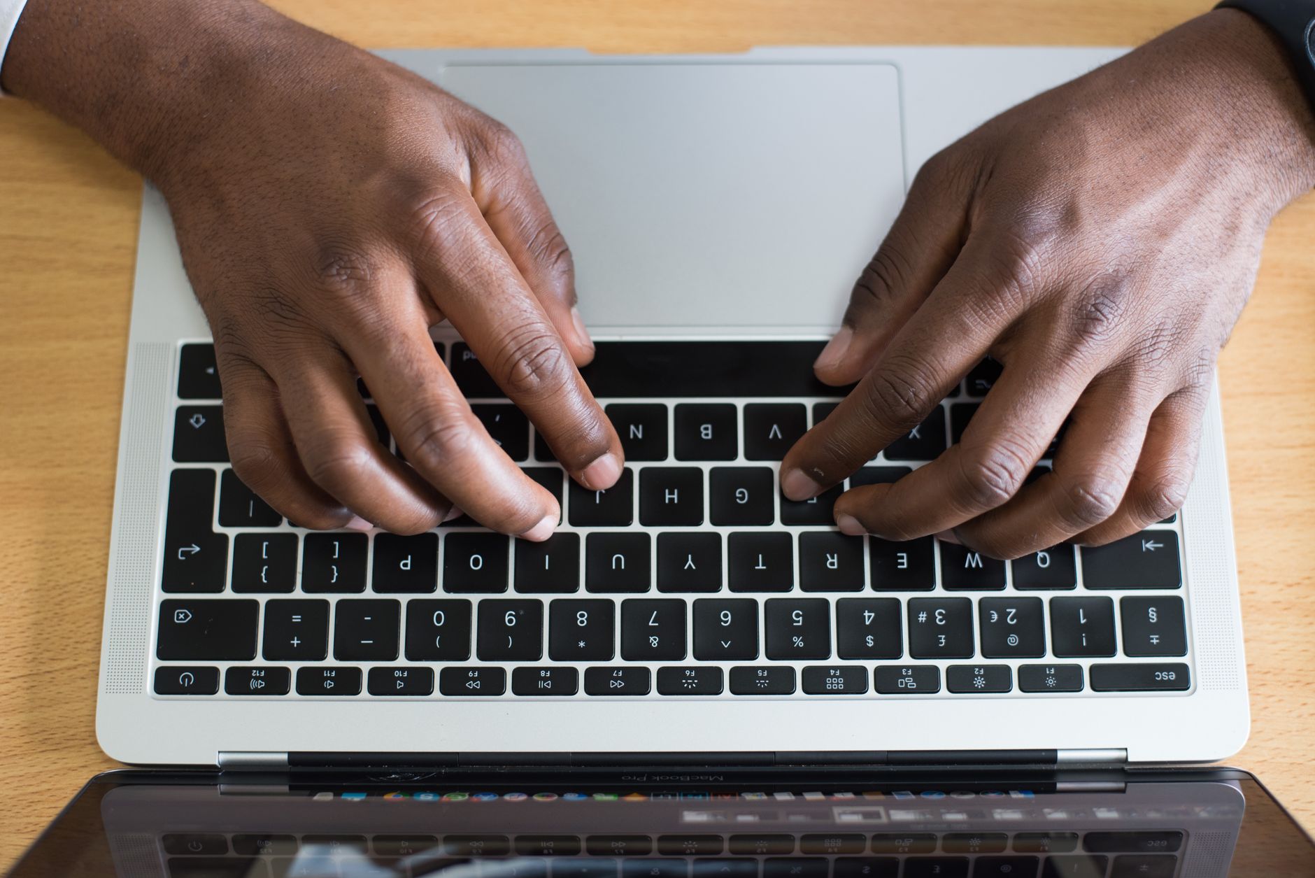 Vue de dessus de deux mains en train de taper sur le clavier d’un ordinateur portable posé sur un bureau en bois.